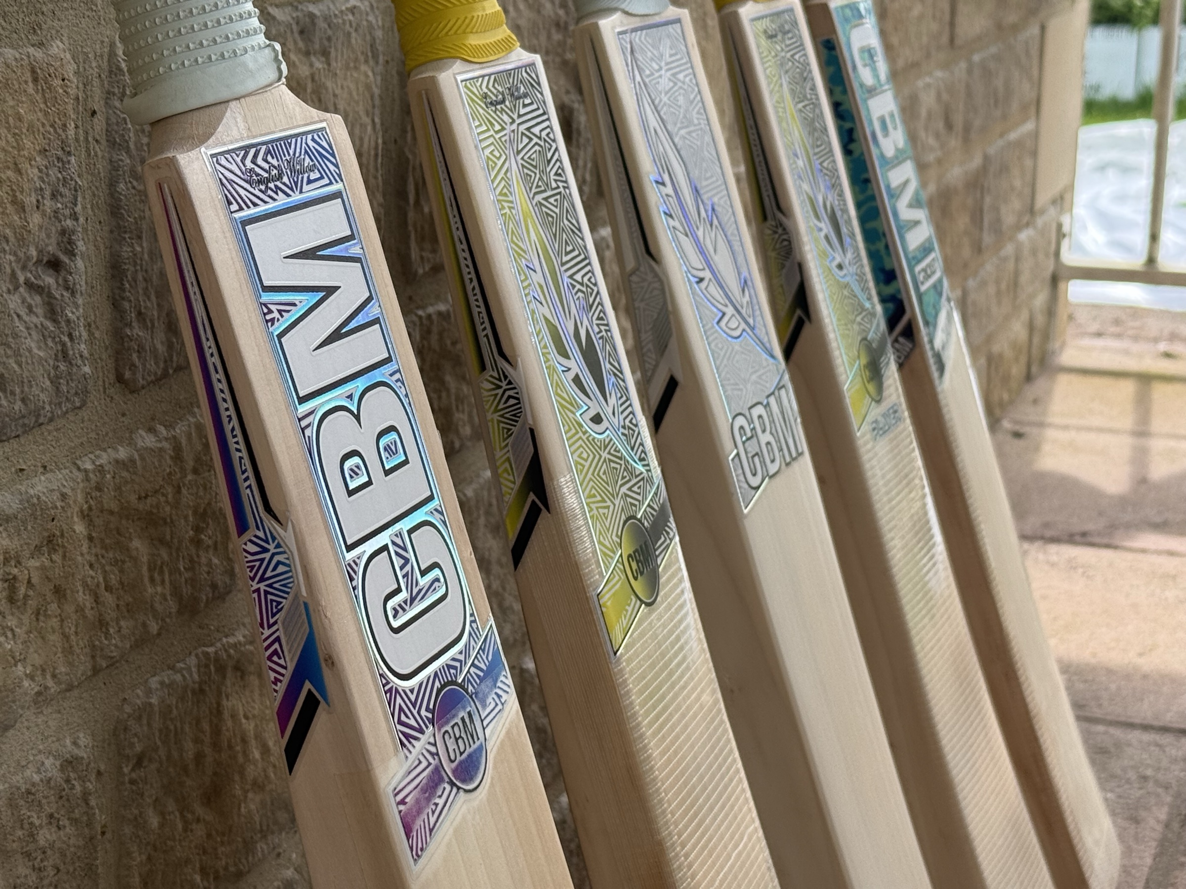 The CBM Cricket bat range, five bats standing against a brick wall.