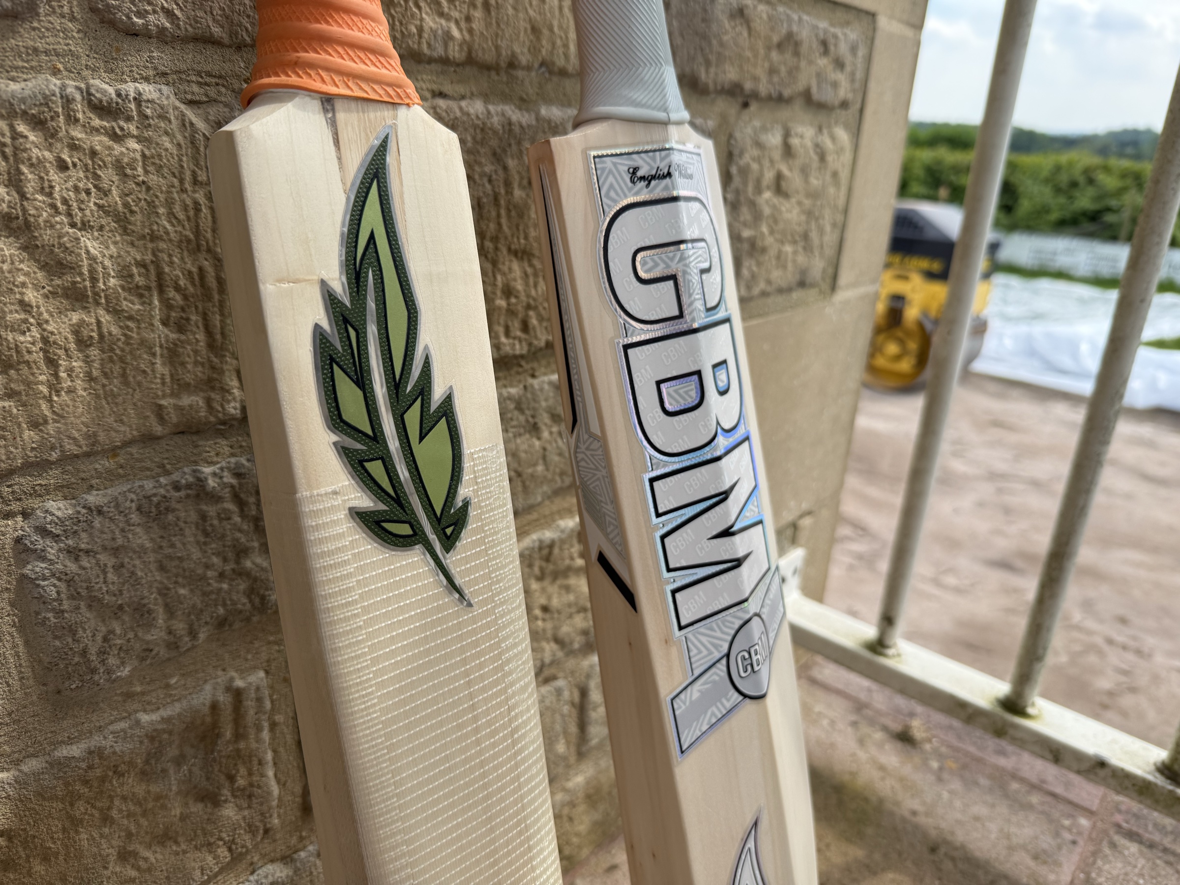 Two CBM cricket bats leaning against a stone wall in the workshop yard.
